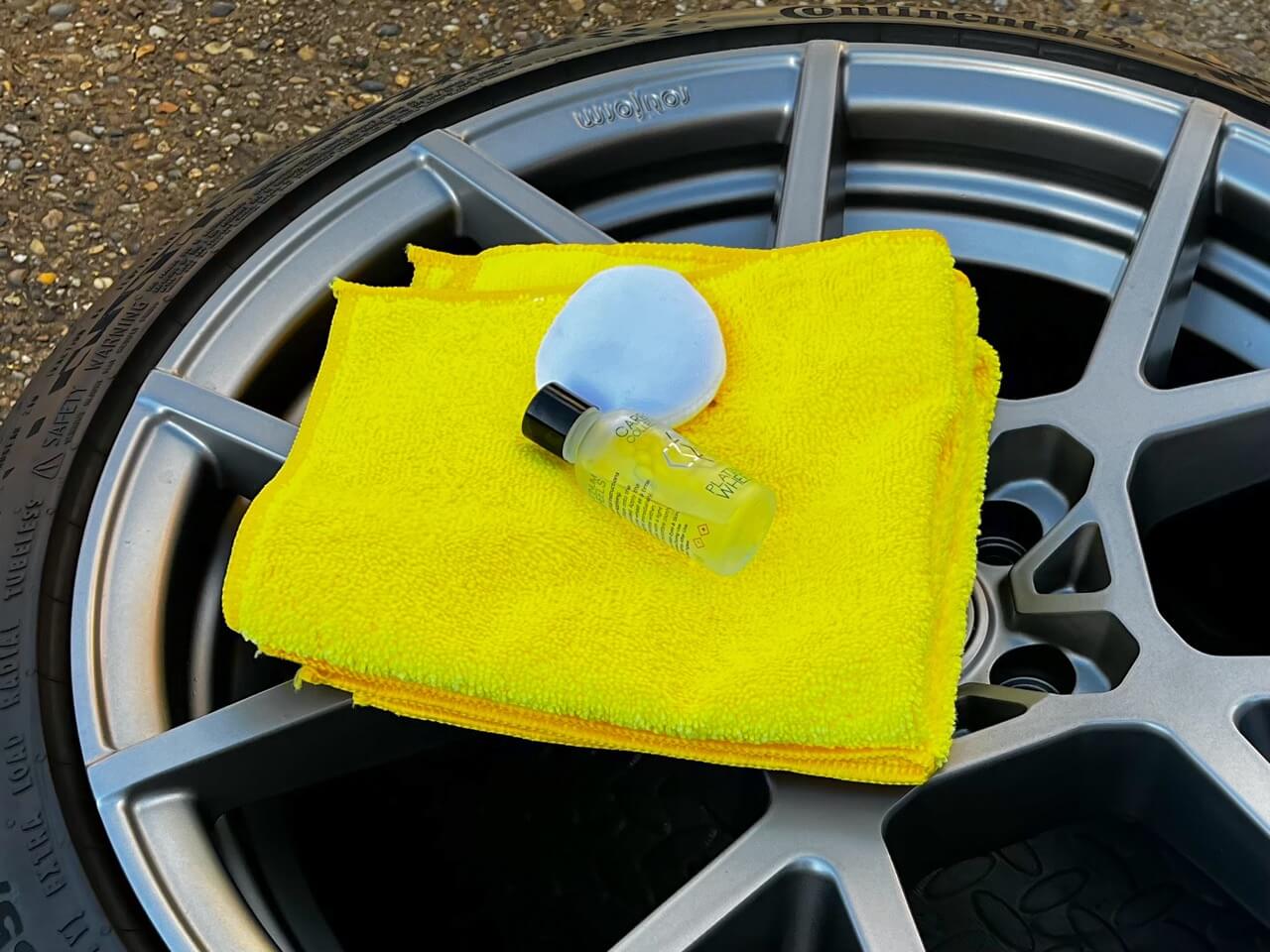 Yellow microfiber cloth with white applicator pad and ceramic coating on top of gray alloy wheel