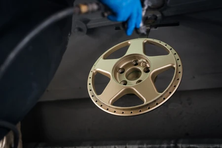 Split rim alloy hanging in the spray booth being painted in the colour gold after being repaired